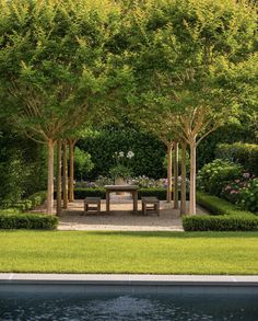 an outdoor dining area is surrounded by trees and shrubs, along with a pool in the foreground