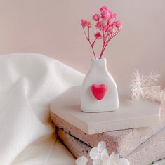 a white vase with pink flowers in it on top of two stacked pieces of paper