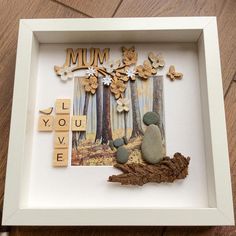 a shadow box with scrabbles, rocks and flowers in it on a wooden floor