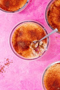 four desserts in glass bowls with spoons on pink background, top view from above