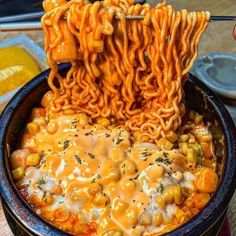 a bowl filled with noodles and cheese being held up by chopsticks over it