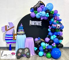 a birthday party with balloons, cake and video game controller on the table in front of a fortnite sign