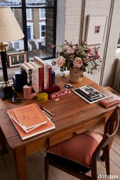 a wooden table topped with books and a vase filled with flowers next to a window