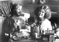 a man and woman sitting at a table with food in front of them, smiling