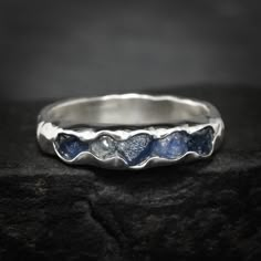 a silver ring with blue stones in the shape of waves on top of a rock