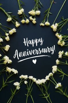 happy anniversary written in white on a black background surrounded by small white flowers and greenery