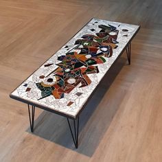 a mosaic table with hairpin legs on the floor in front of a wood floor