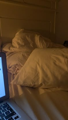 an open laptop computer sitting on top of a bed next to pillows and pillow cases