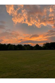 a field with trees and clouds in the background at sunset or sunrise hours before dawn