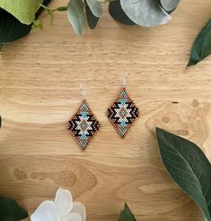 a pair of beaded earrings sitting on top of a wooden table next to flowers