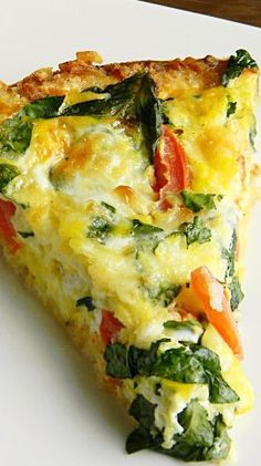 a slice of quiche on a white plate with spinach and tomato toppings