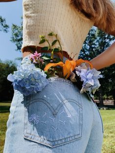 a woman is holding her back with flowers in it's pocket and jeans on the side