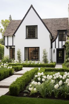 a white house with black trim and windows surrounded by greenery in front of it