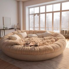 a living room with a large round couch in the middle of it and windows looking out onto snow covered trees