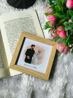 an open book next to a bouquet of pink roses and a photo frame on a furry surface