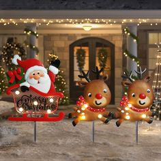 three christmas yard decorations in front of a house decorated with lights and santa claus on his sleigh