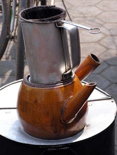 an old coffee pot is sitting on top of a metal stand with a pipe sticking out of it