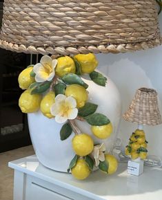 a white vase with lemons and flowers sitting on a table next to a lamp