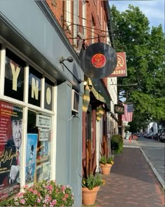 an empty sidewalk in front of a building with signs on the windows and flowers growing outside