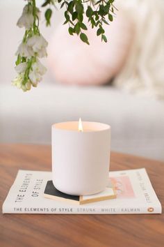 a white candle sitting on top of a wooden table next to a book and flowers