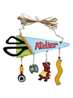 a sign that says atelier hanging from a string with scissors and other items attached to it