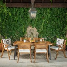 an outdoor dining table and chairs in front of a green wall