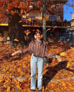 a woman wearing headphones standing under a street sign surrounded by autumn leaves and trees