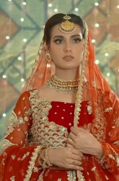 a woman in a red and gold bridal outfit with her hands on her chest