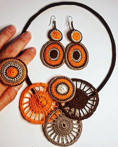 a hand is holding an orange and brown necklace and earring set