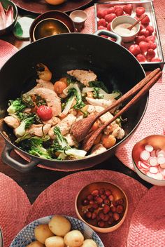 a pan filled with meat and vegetables on top of a red table cloth next to other dishes