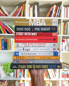 a person holding a stack of books in front of a book shelf full of books