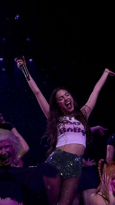 a woman with her arms in the air while performing on stage at a concert or show