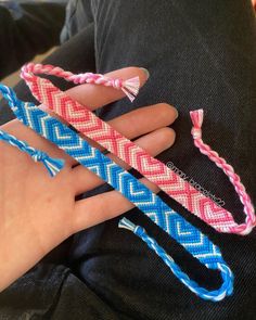 someone is holding two different colored bracelets on their fingers and one has a pink, blue, and white braided handle