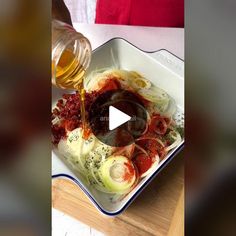 someone is pouring sauce on some food in a white bowl with red onions and other ingredients