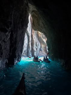 several people in boats are floating through the water inside a cave with blue light coming from its entrance