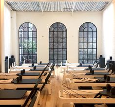 rows of yoga mats lined up in an empty room with large windows and wooden floors