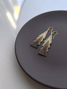 a pair of gold and silver earrings sitting on top of a black plate next to a white table