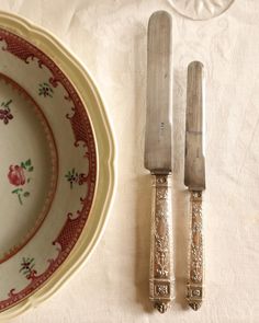 two knives and a fork sitting on top of a white table cloth next to a plate