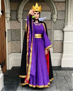 a woman wearing a purple and black costume with a crown on her head, standing in front of a doorway