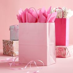 pink gift bags with ribbons and bows on them sitting next to each other in front of a pink background