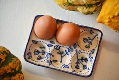 two eggs in a blue and white dish next to gourds