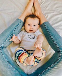 a baby sitting on top of a bed with his hands in the air and looking at the camera