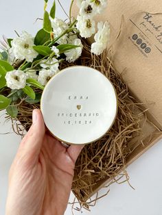 a hand holding a personalized ring dish next to flowers