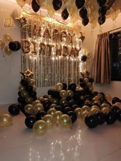 black and gold balloons are on the floor in front of a happy birthday sign with streamers