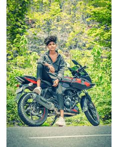 a man sitting on top of a motorcycle in the middle of a road next to trees