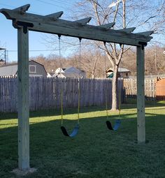 a wooden swing set in the backyard with two swings attached to it's posts