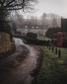 a red phone booth sitting on the side of a road next to a lush green field