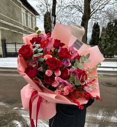 a bouquet of red roses wrapped in pink paper and tied to a black post on the street