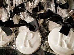 some white cookies wrapped in black ribbon on top of plastic wrappers with monogrammed letters