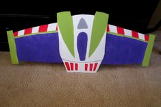 a paper model of a green, white and purple plane on the floor next to a black wall